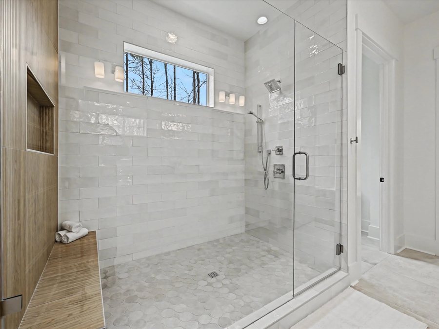 Primary shower with tile run to the ceiling, a teak bench, and a clerestory window to the pines.