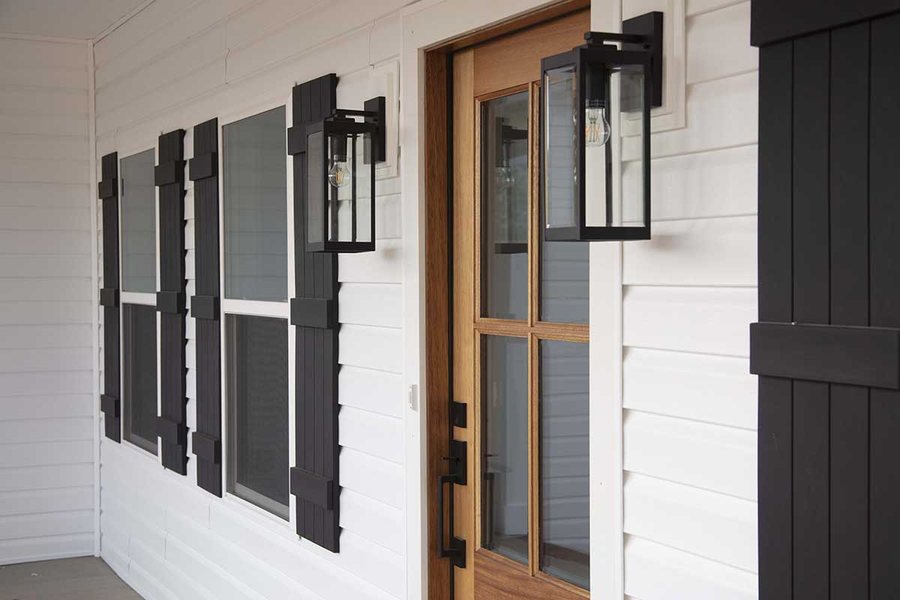 Porch detail: stained wood entry door, black board and batten shutters, and lantern sconces.