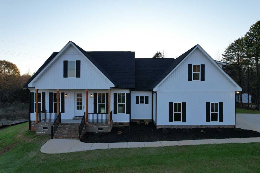 White farmhouse style custom home with black shutters and a covered front porch at dusk.