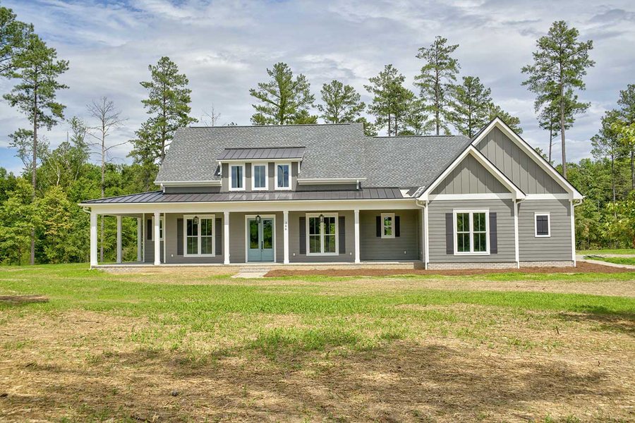 Grey custom home with a wraparound porch, standing seam metal roof accent, and a dormer.