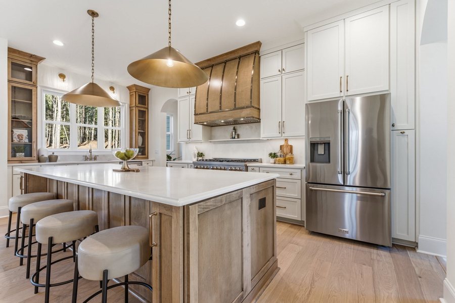 Kitchen with a white oak island, brass pendants, panelled hood, and a wall of windows to the treeline.