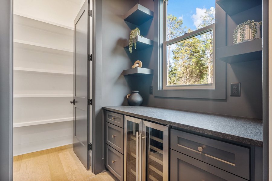 Scullery with navy cabinetry, floating shelves, twin wine refrigerators, and a walk in pantry beyond.
